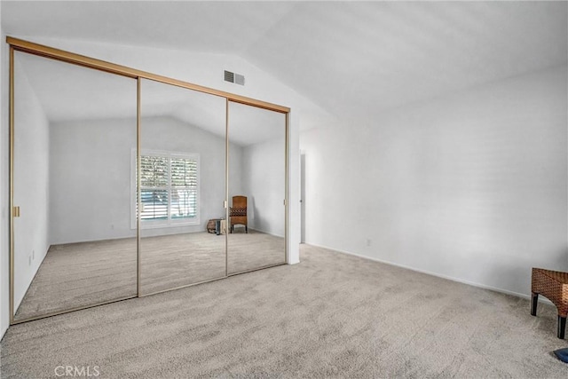 unfurnished bedroom with lofted ceiling, a closet, visible vents, and light carpet