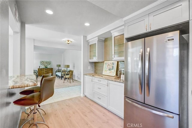 kitchen featuring light stone counters, light wood-style flooring, white cabinetry, freestanding refrigerator, and glass insert cabinets