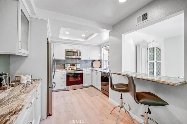 kitchen featuring visible vents, appliances with stainless steel finishes, a peninsula, a kitchen bar, and white cabinetry