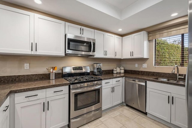 kitchen featuring white cabinetry, appliances with stainless steel finishes, light tile patterned flooring, dark stone counters, and sink