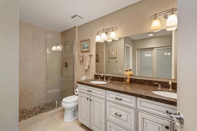 bathroom featuring toilet, vanity, tile patterned floors, and a tile shower