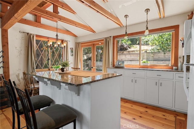 kitchen featuring decorative light fixtures, a breakfast bar, white cabinets, and lofted ceiling with beams