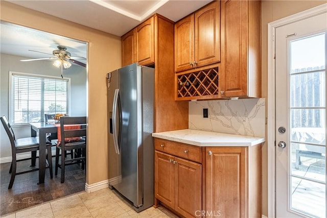 kitchen with light stone countertops, backsplash, stainless steel fridge, light tile patterned flooring, and ceiling fan