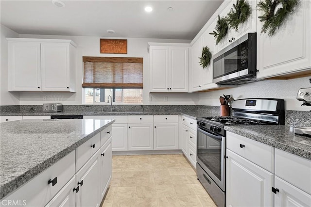 kitchen with appliances with stainless steel finishes, sink, stone counters, and white cabinetry