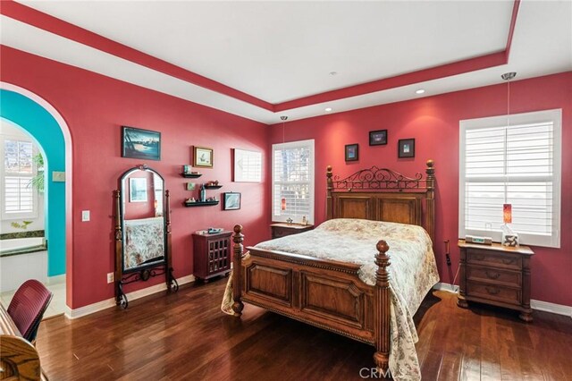 bedroom featuring ensuite bath, dark hardwood / wood-style floors, and a raised ceiling