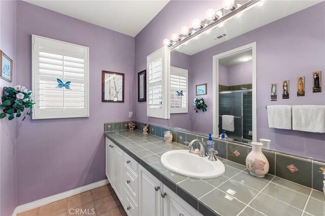 bathroom with a shower with door, vanity, and tile patterned flooring