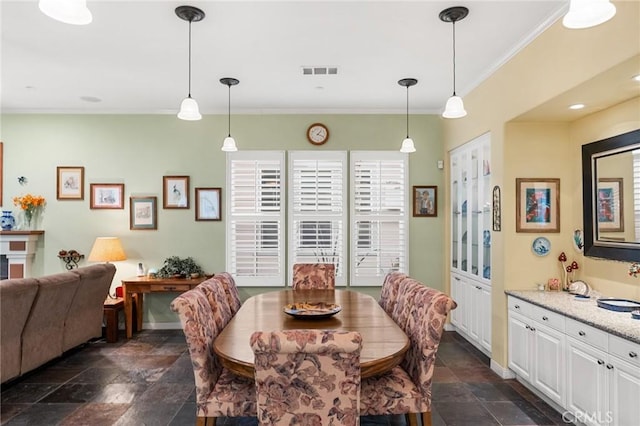 dining room featuring stone tile floors, visible vents, baseboards, and crown molding