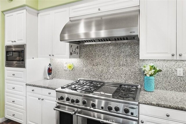 kitchen with light stone counters, extractor fan, white cabinets, and appliances with stainless steel finishes