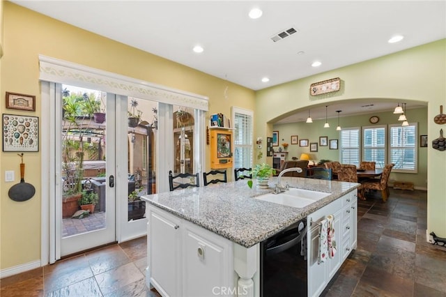 kitchen with arched walkways, a sink, visible vents, white cabinetry, and a center island with sink