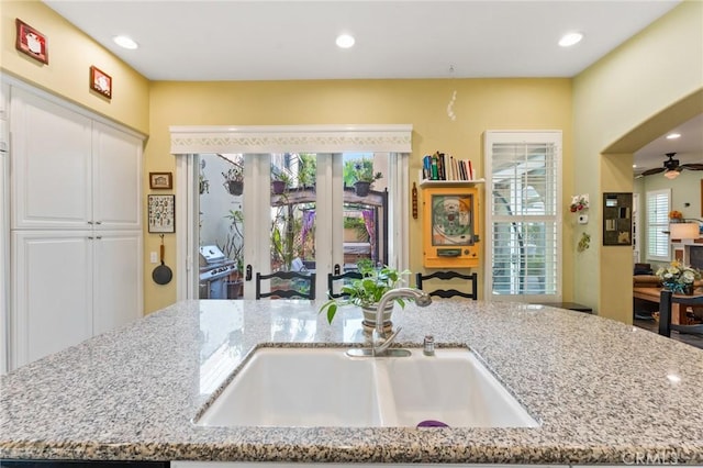 kitchen with an island with sink, light stone countertops, a sink, and recessed lighting