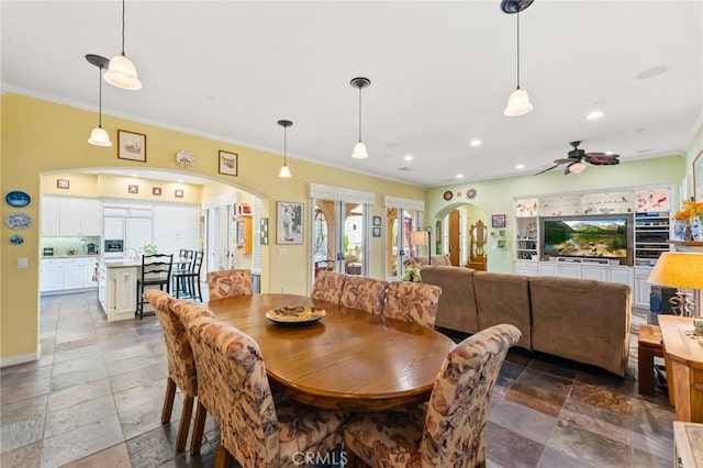 dining room featuring arched walkways, ceiling fan, recessed lighting, stone tile flooring, and crown molding