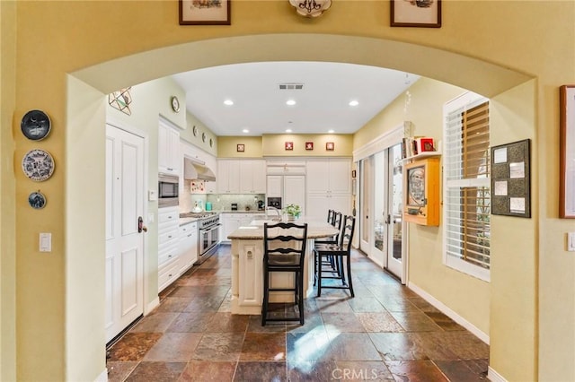 kitchen with arched walkways, stainless steel appliances, a breakfast bar, and a kitchen island