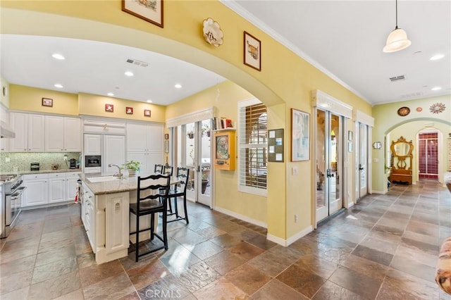 kitchen featuring a kitchen bar, light stone counters, white cabinetry, stainless steel range, and a kitchen island with sink