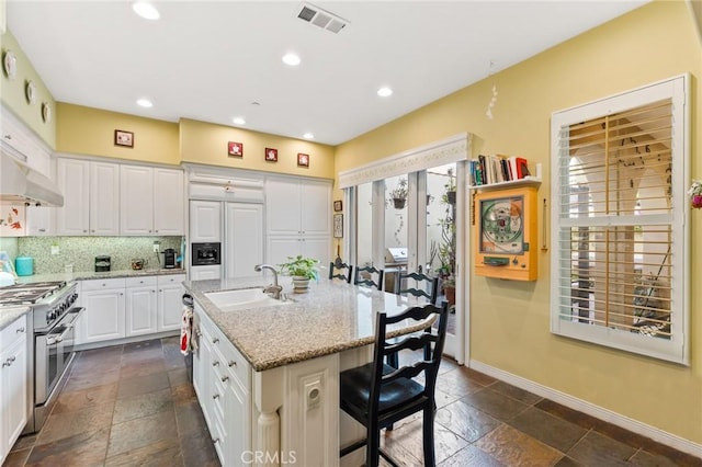 kitchen featuring stainless steel stove, visible vents, white cabinetry, a sink, and an island with sink