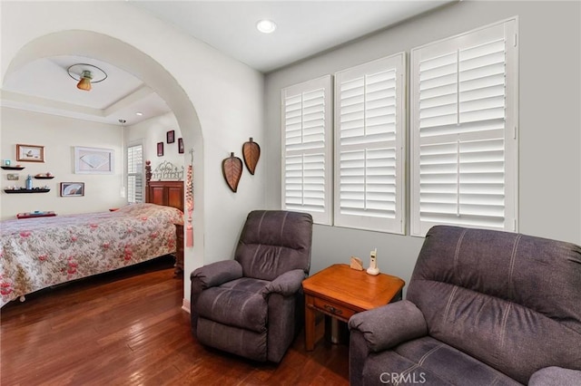 bedroom with dark wood-style floors, arched walkways, a raised ceiling, and recessed lighting