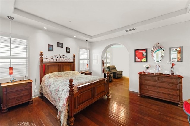 bedroom with arched walkways, dark wood-style flooring, a raised ceiling, visible vents, and baseboards