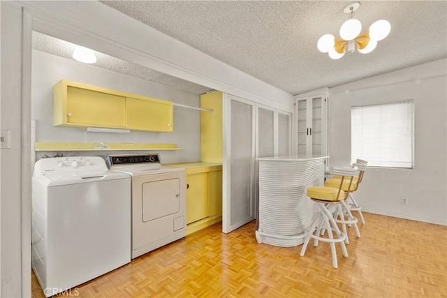 washroom with an inviting chandelier, light parquet floors, washing machine and clothes dryer, a textured ceiling, and cabinets