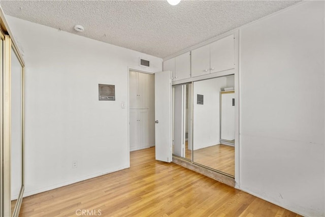 unfurnished bedroom featuring light hardwood / wood-style floors, a textured ceiling, and a closet