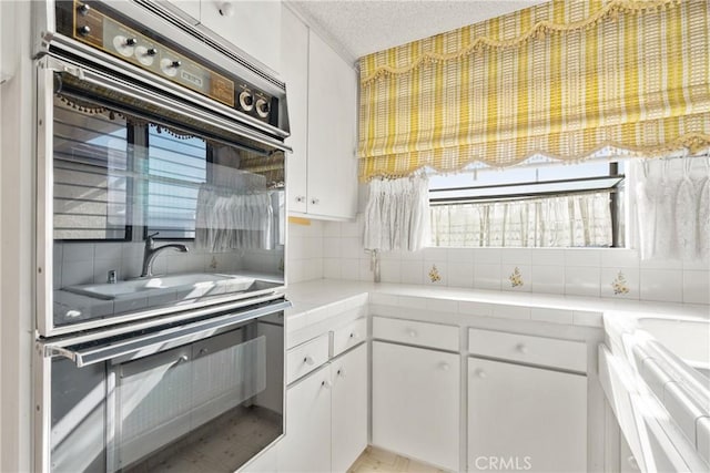 kitchen featuring a textured ceiling, white cabinets, double oven, and tasteful backsplash