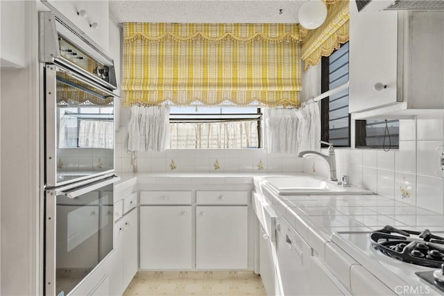 kitchen featuring white cabinetry, tile countertops, stainless steel double oven, tasteful backsplash, and sink