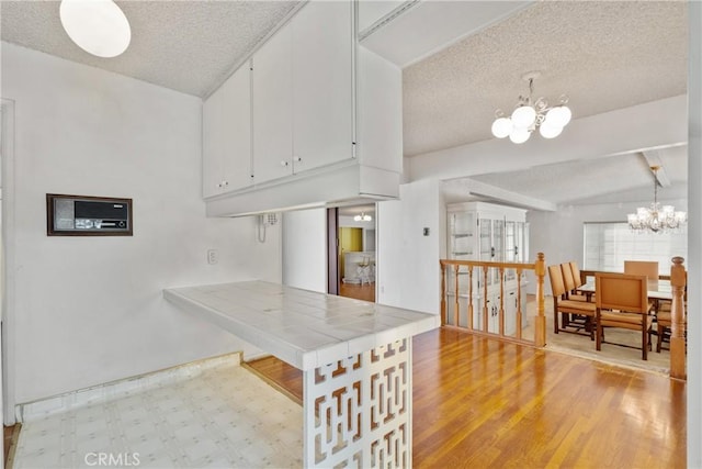 kitchen with a notable chandelier, kitchen peninsula, white cabinetry, hanging light fixtures, and tile counters