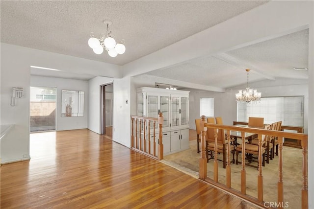 dining space featuring light wood-type flooring, lofted ceiling with beams, an inviting chandelier, and a textured ceiling