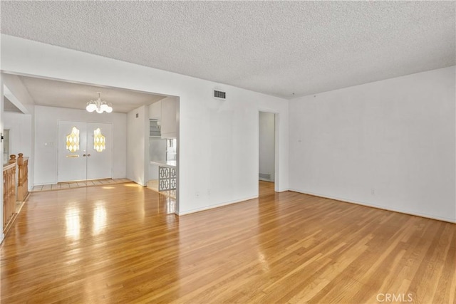 empty room featuring light hardwood / wood-style floors, a textured ceiling, and an inviting chandelier