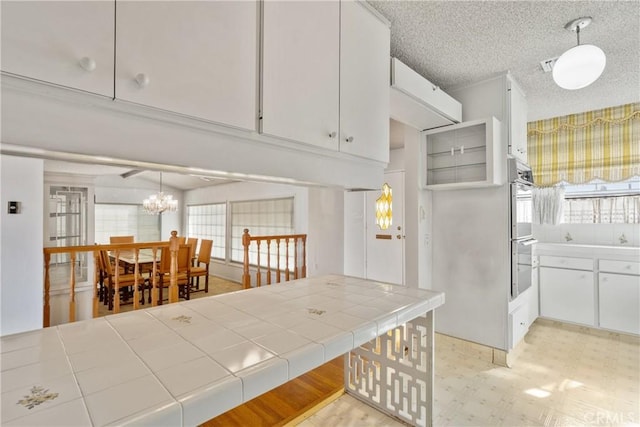 kitchen with pendant lighting, a textured ceiling, tile counters, white cabinetry, and a chandelier