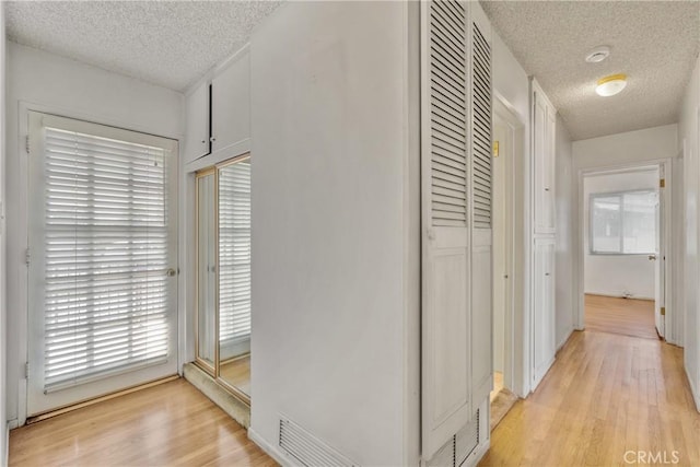 corridor with a textured ceiling and light hardwood / wood-style floors