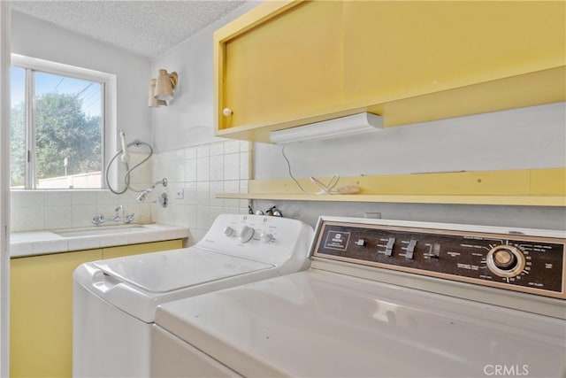 laundry area with cabinets, a textured ceiling, sink, and washing machine and dryer