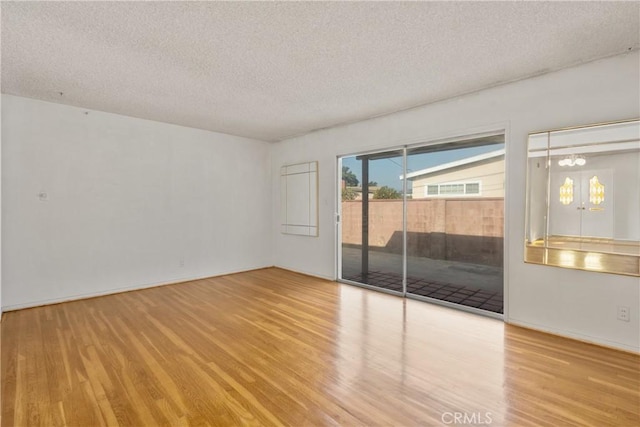 empty room featuring a textured ceiling, a chandelier, and light wood-type flooring