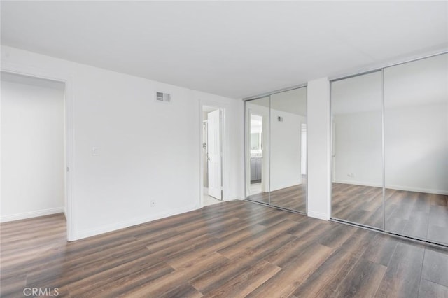 unfurnished bedroom with dark hardwood / wood-style flooring and multiple closets