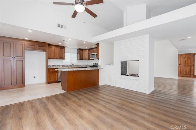 kitchen with light stone countertops, a towering ceiling, a fireplace, ceiling fan, and light hardwood / wood-style flooring