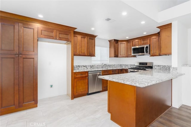 kitchen with kitchen peninsula, appliances with stainless steel finishes, light stone counters, and sink