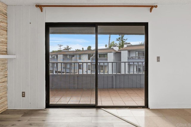 doorway to outside with light hardwood / wood-style floors, a textured ceiling, and wood walls