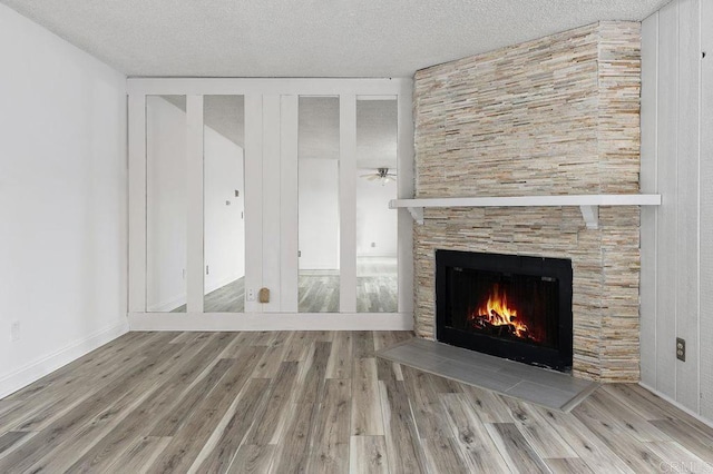 unfurnished living room featuring wood-type flooring, a textured ceiling, and a stone fireplace