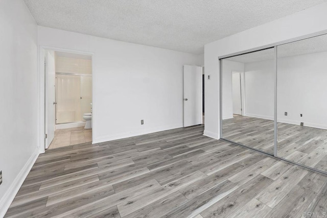 unfurnished bedroom featuring baseboards, a closet, a textured ceiling, and wood finished floors