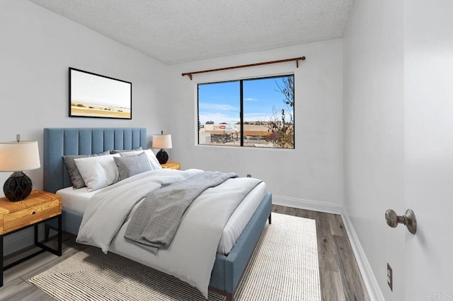 bedroom with baseboards, a textured ceiling, and wood finished floors