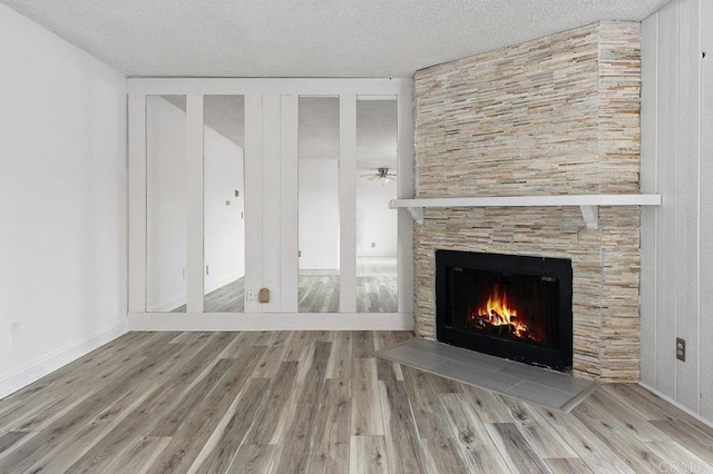unfurnished living room featuring a tiled fireplace, ceiling fan, a textured ceiling, and wood finished floors
