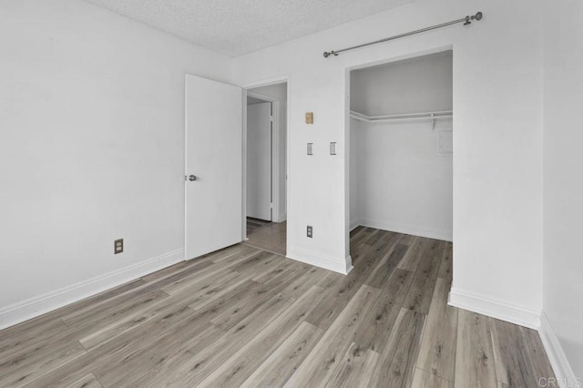 unfurnished bedroom featuring a textured ceiling, a closet, baseboards, and wood finished floors