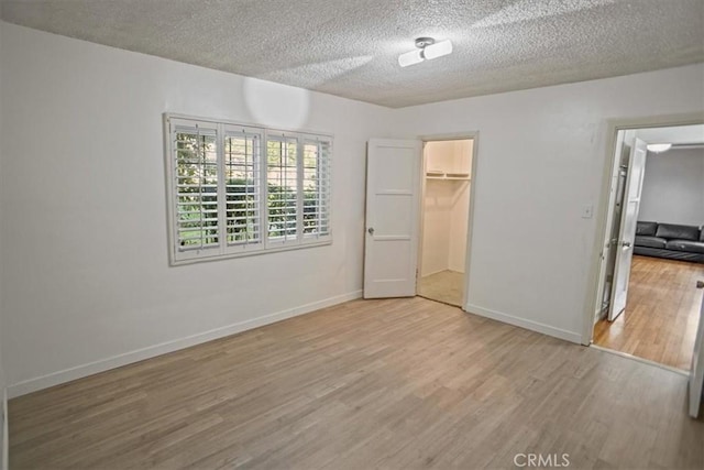 unfurnished bedroom with a spacious closet, a closet, a textured ceiling, and light wood-type flooring