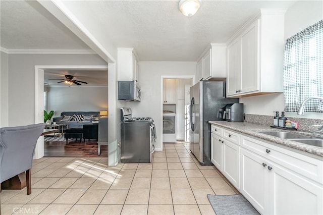 kitchen with appliances with stainless steel finishes, washer / clothes dryer, white cabinetry, sink, and ceiling fan