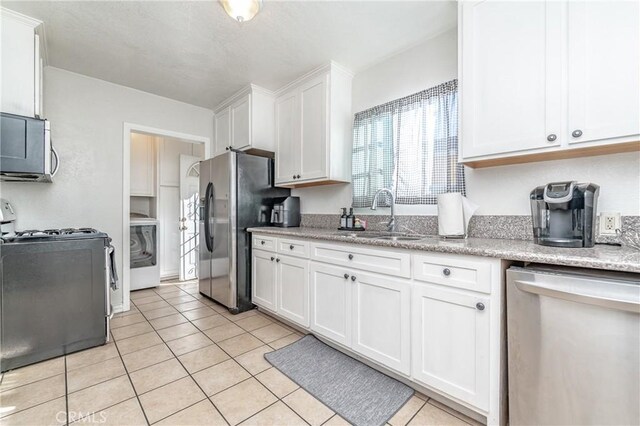 kitchen with washer / dryer, appliances with stainless steel finishes, white cabinets, and sink