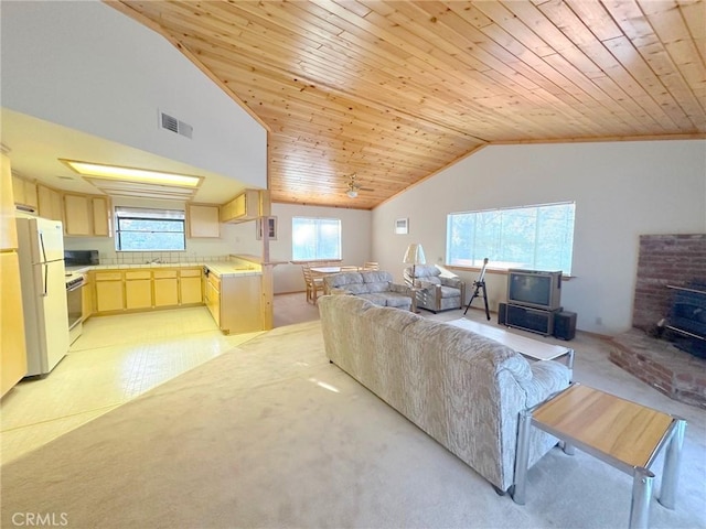 carpeted living room with lofted ceiling, a wood stove, sink, ceiling fan, and wooden ceiling