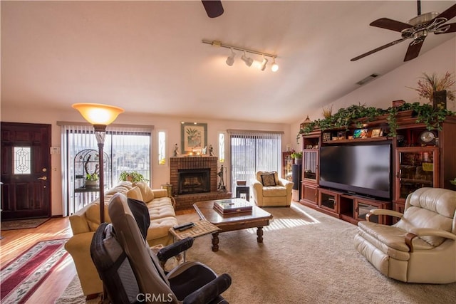 living room with track lighting, a fireplace, ceiling fan, vaulted ceiling, and hardwood / wood-style flooring