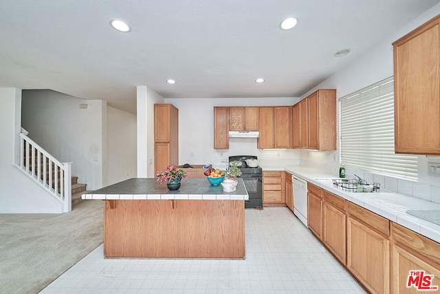 kitchen with tile counters, gas stove, a kitchen breakfast bar, dishwasher, and a center island