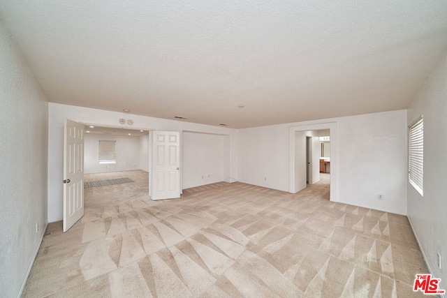 empty room with light colored carpet and a textured ceiling