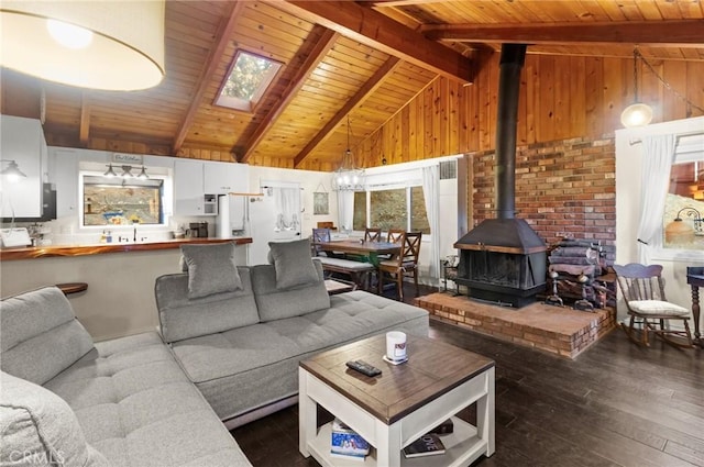 living room featuring a skylight, a wood stove, dark wood-type flooring, high vaulted ceiling, and beam ceiling