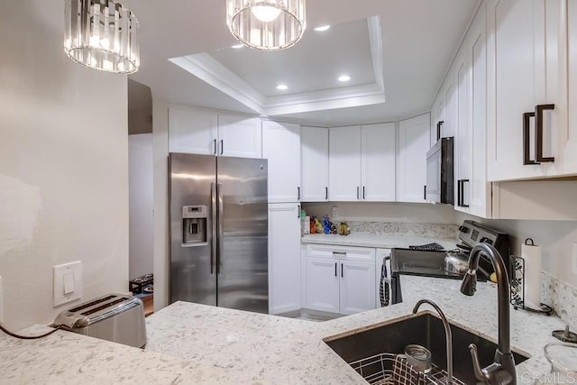 kitchen with a raised ceiling, appliances with stainless steel finishes, white cabinetry, and a notable chandelier