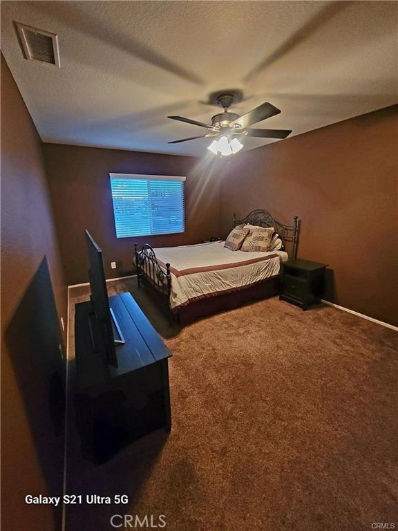 carpeted bedroom featuring ceiling fan and a textured ceiling